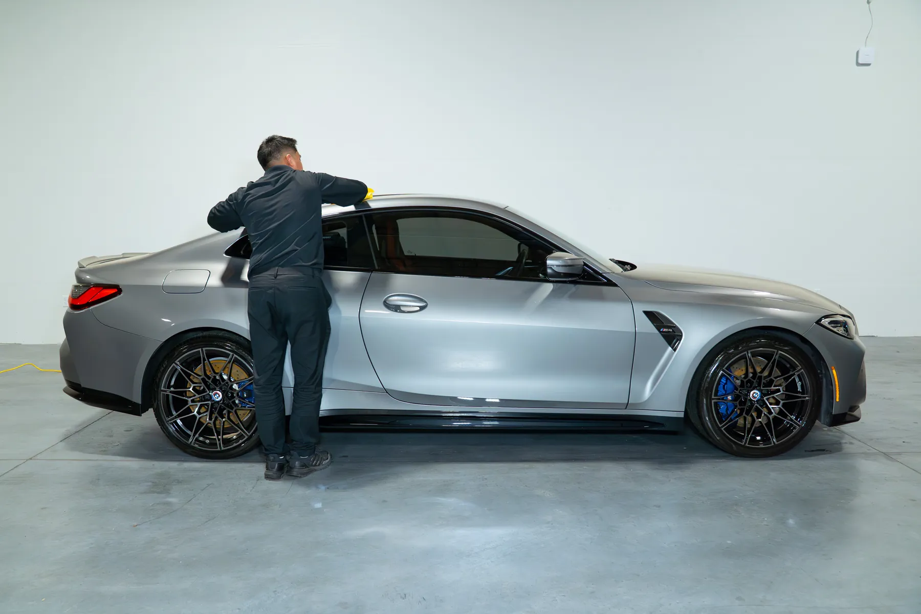 A technician wiping down a silver BMW M4 inside the coating bay