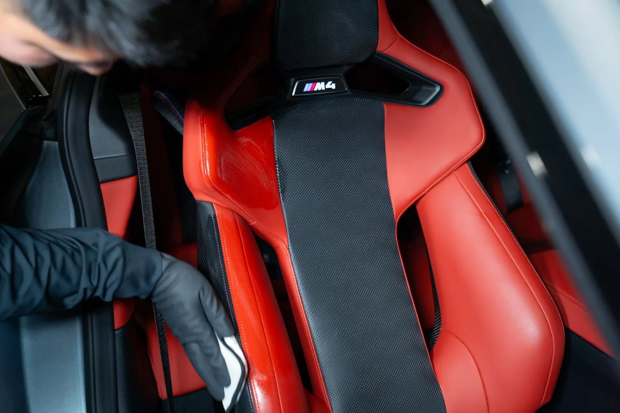 A technician cleaning the red and black leather seats of a BMW M4