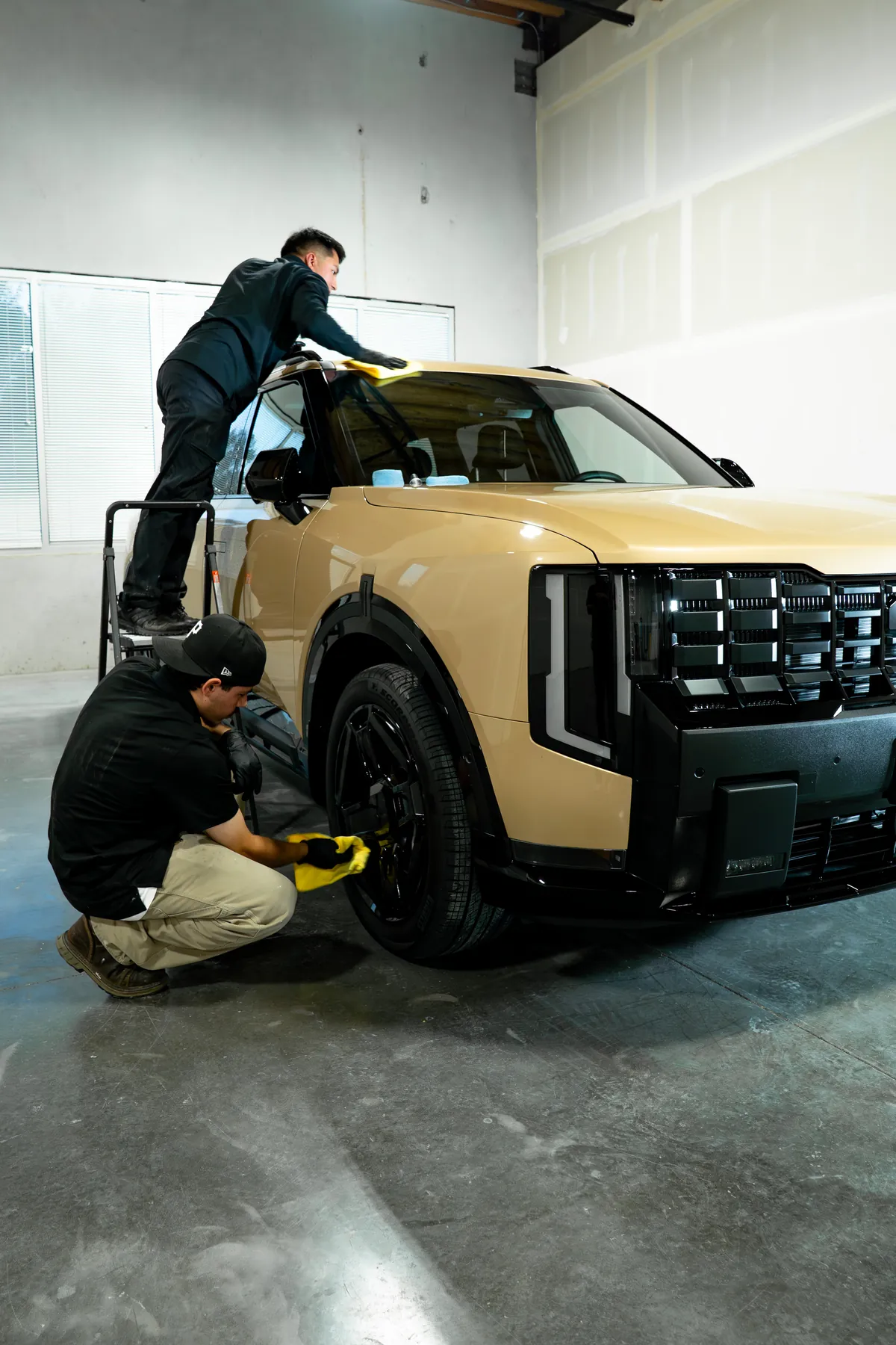 A technician coating the flank of a tan Kia EV9 inside the studio