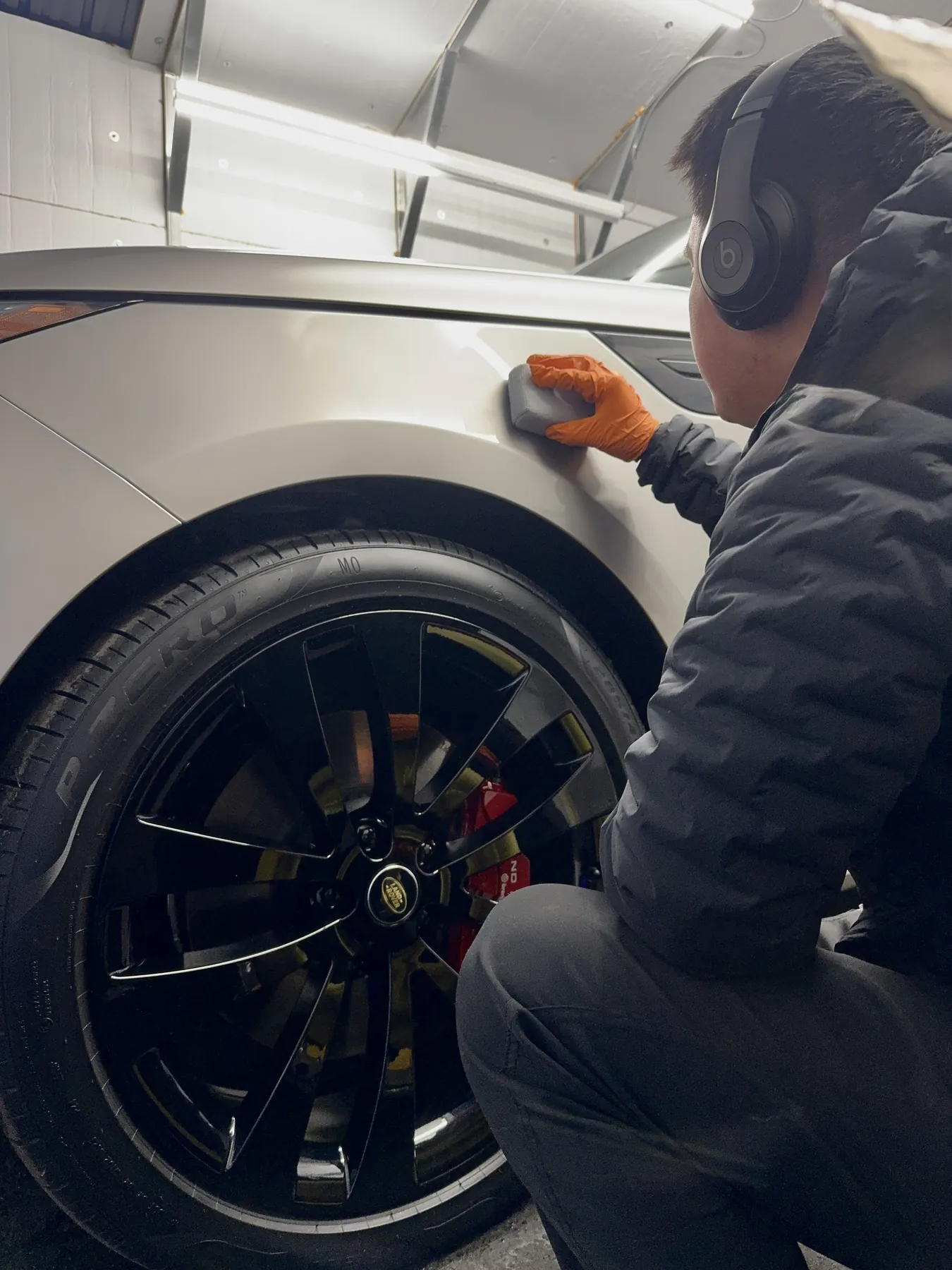 A technician applying coating to the bodywork around a Porsche wheel
